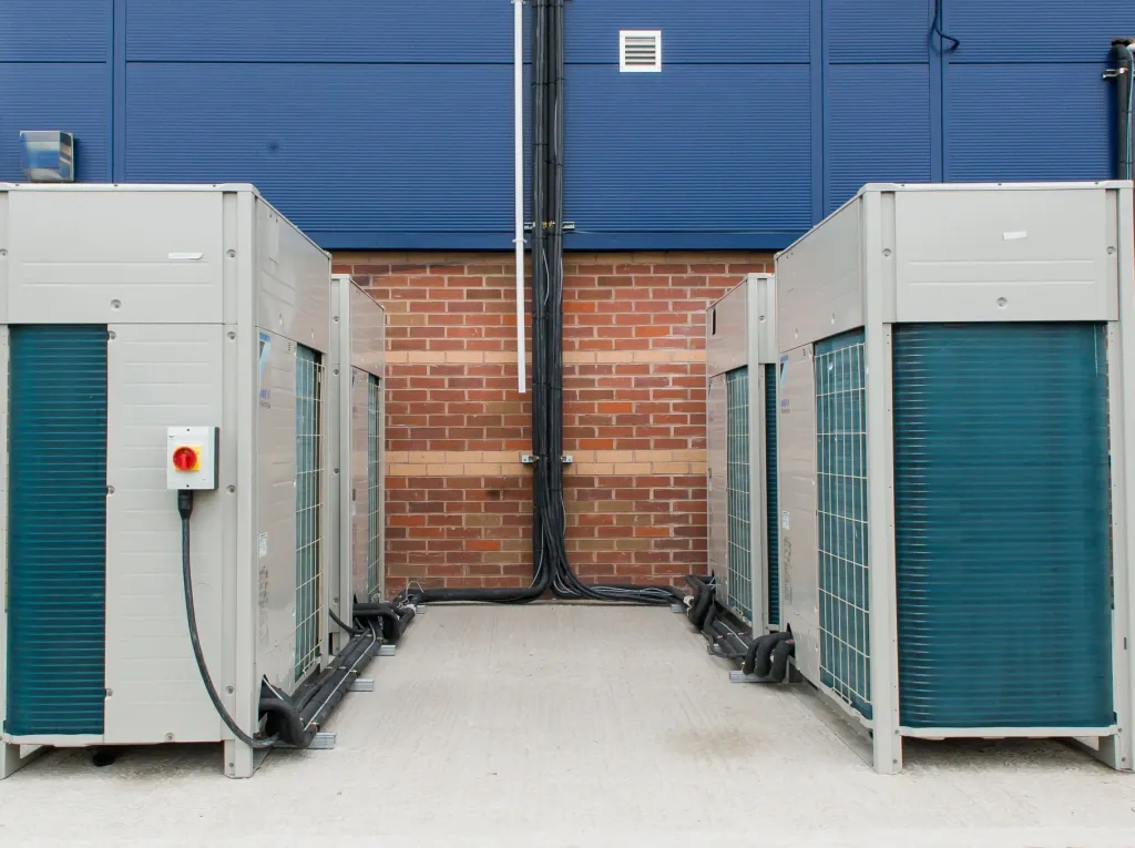 VRV / VRF systems for large commercial buildings Bank of VRF outdoor condenser units installed against a commercial building — the multi-zone heat-pump platform AccuTemp specifies for multi-floor sites