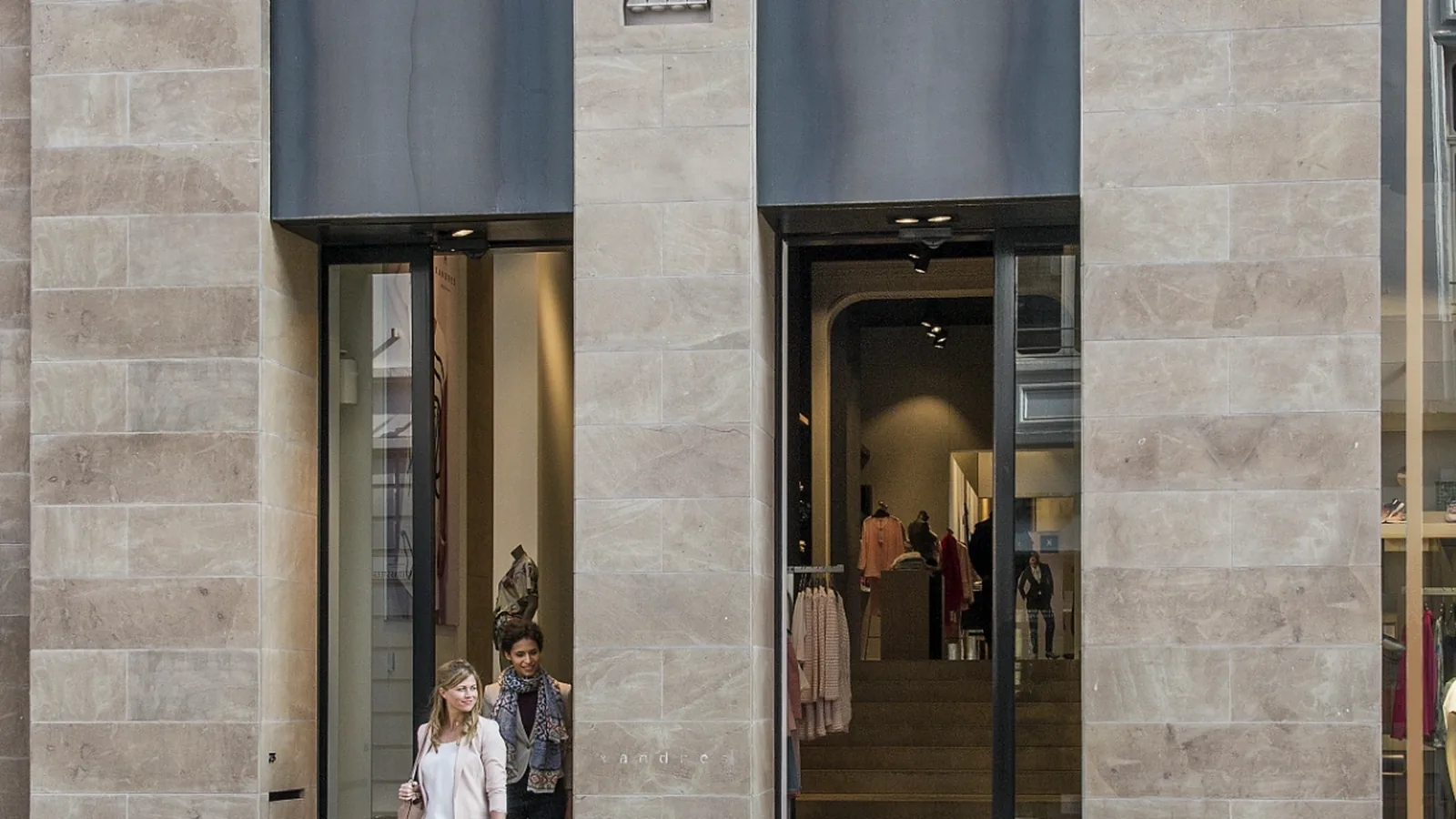 Shoppers exiting a high-street retail unit under an over-door air curtain — AccuTemp commercial retail air conditioning engineered to control door-open heat gain and keep the shop trading with the door open.